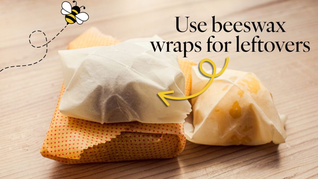 10 Easy Swaps for a More Sustainable Lifestyle 1 A stack of food items wrapped in beeswax wraps for food storage, placed on a wooden surface. A yellow polka-dotted wrap with red dots is at the bottom, followed by a plain beige wrap, and a wrap with visible cheese inside on top. A small bee illustration with a dotted trail is in the top left corner. Text on the right reads, "use beeswax wraps for leftovers," with a yellow arrow pointing to the wraps, which references a recommendation for a sustainable lifestyle swap.
